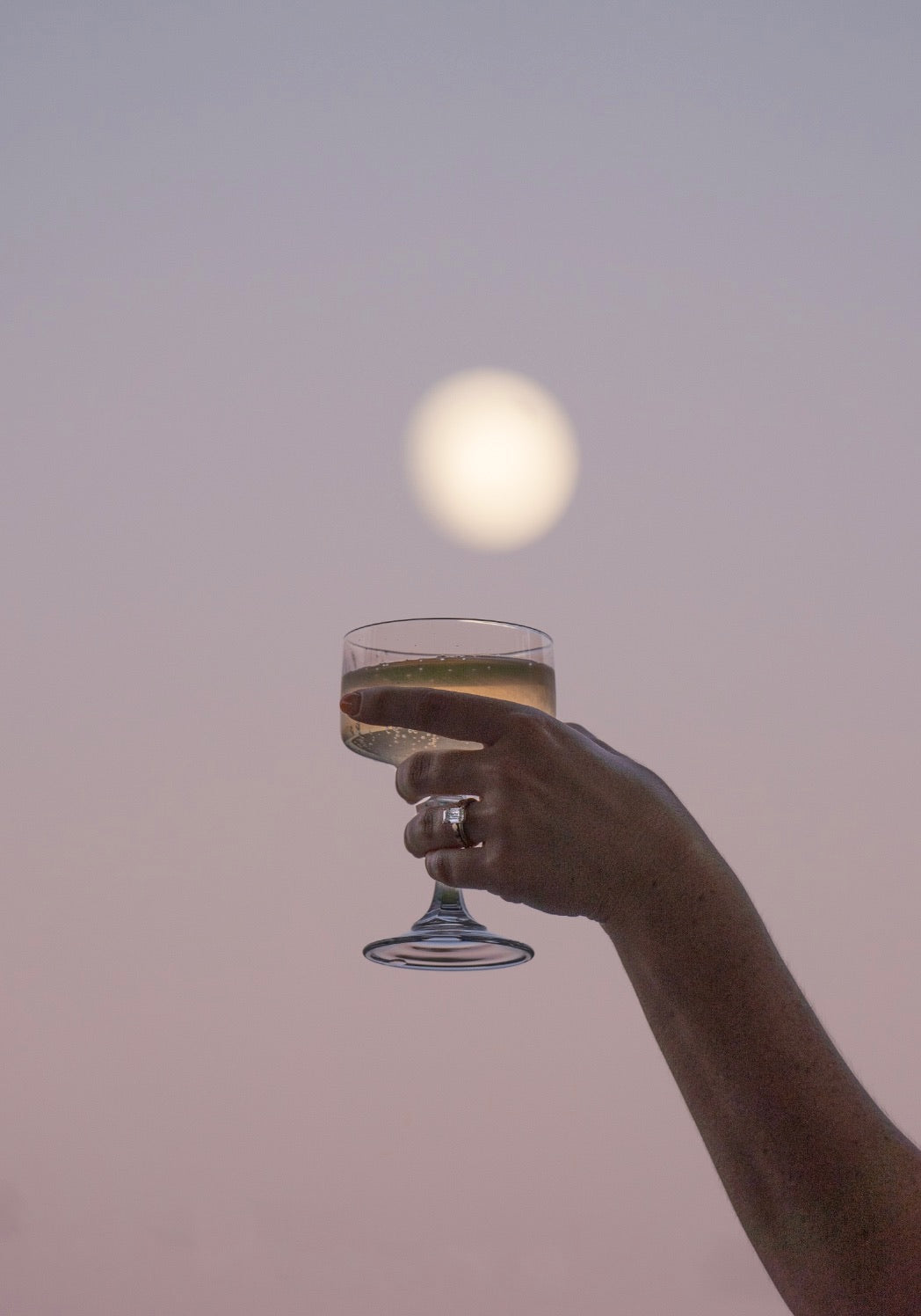 Hand holding a glass with a drink against a twilight sky